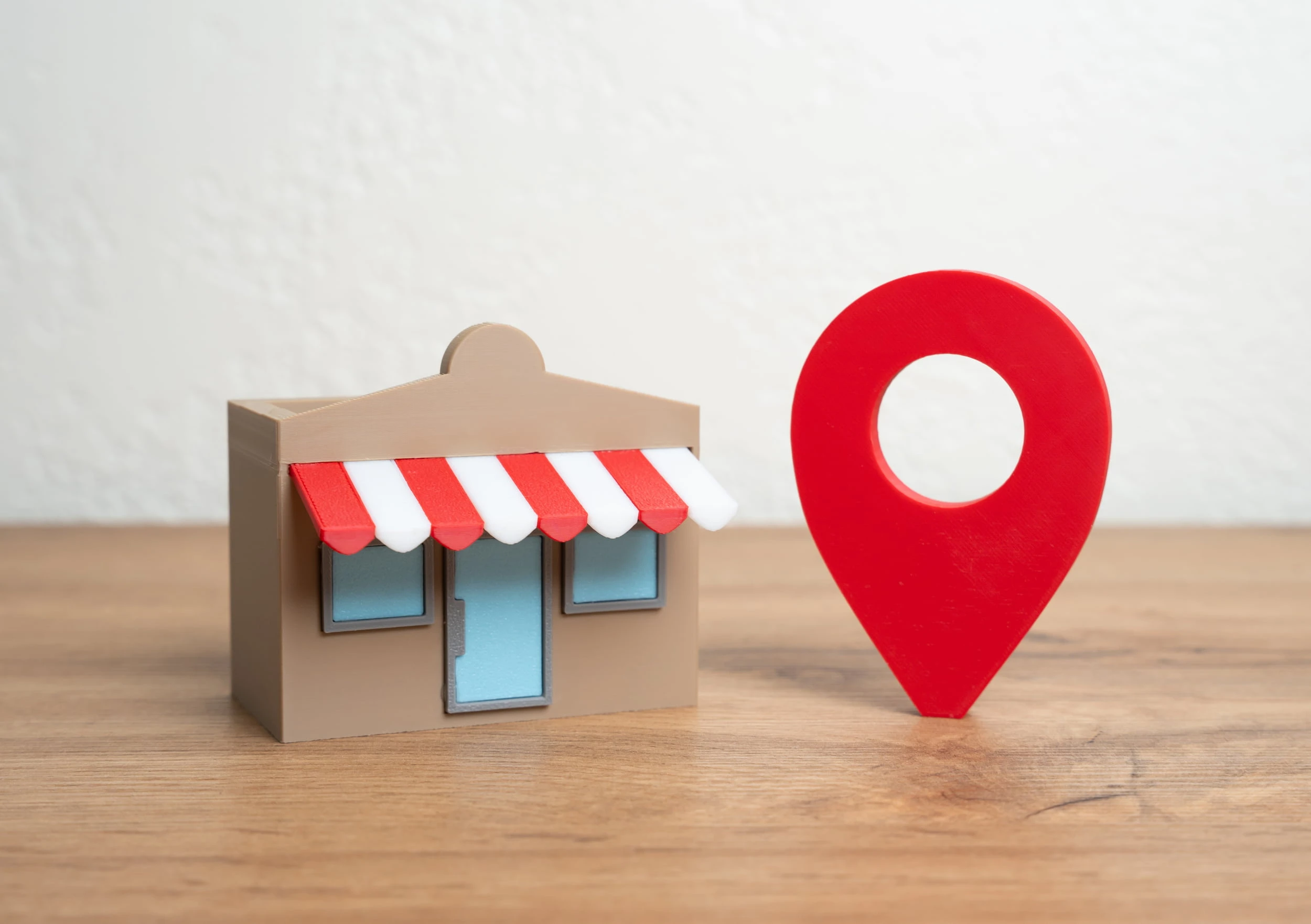 A small model storefront next to a red map location pin, representing local map visibility